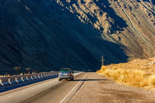 Car is driving along the road to Issyk-Kul lake through natural Kyrgyzstan mountain landscape with concrete barrier at sunny autumn day.
