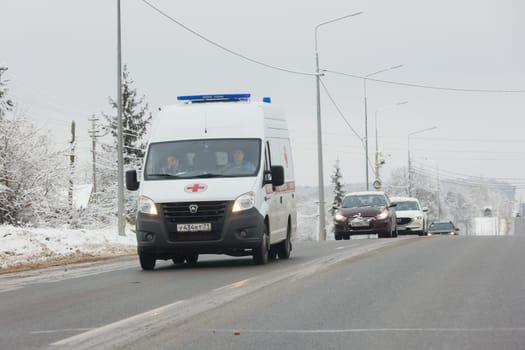 white ambulance minibus with two women inside the cabin driving along winter road at cloudy day in Tula, Russia - December 9. 2021