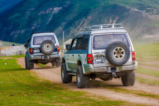Two old SUVs on rugged mountain ravine road, leaving dusty paths, symbolizing adventure and exploration in nature in Semenovskoye gorge, Kyrgyzstan at July 5, 2023