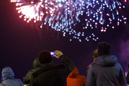 group of unrecognizable people in warm clothes are watching fireworks in a night sky, rear view