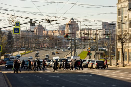 pedestrians crossing road in front of cityscape at sunny morning in Tula, Russia - October 23, 2021