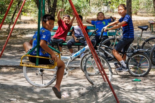 Kyrgyz boys sitting at playground with a bicycles at sunny summer day in Tokmok, Kyrgyzstan - June 30, 2023
