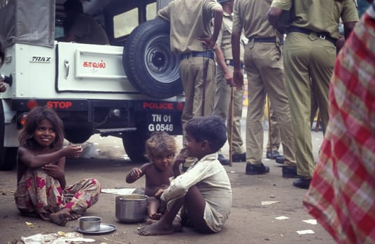 poor children with some food in front of a group of police men on a square in the city of Chennai in Province Tamil Nadu in India.  India, Chennai, April, 1998