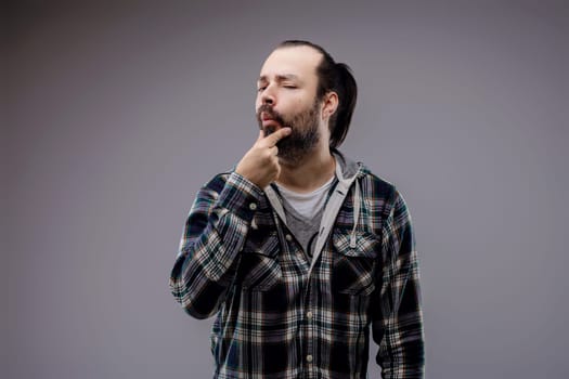 Young man deep in thought, touching his beard, looking uncertain and contemplative in a studio shot