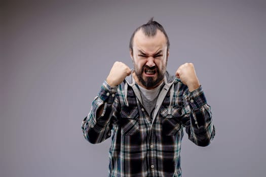 Aggressive man with a beard is clenching his fists and showing his teeth in anger. He is expressing negative emotions with an aggressive attitude