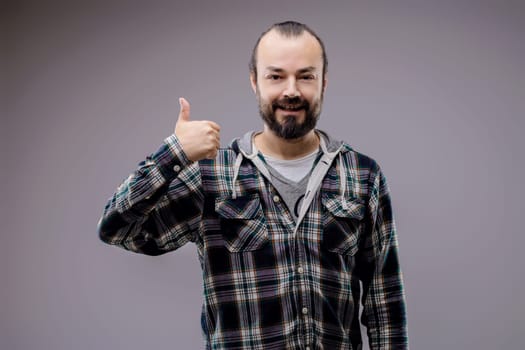 Bearded man in a green plaid shirt smiles and gives a thumbs up, radiating positivity and confidence. Perfect for conveying success and approval