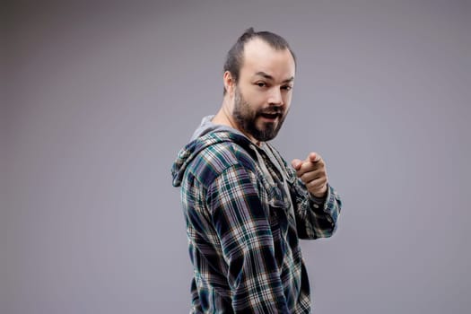 Bearded man in a casual shirt happily points off camera, inviting you to join in the fun with his warm and playful gesture