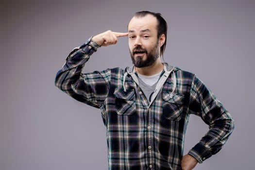 Bearded man is pointing at his temple with his index finger while slightly opening his mouth, expressing thought and concentration