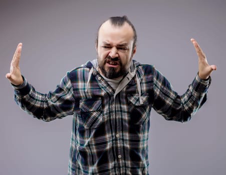 Bearded man is expressing frustration and anger while raising his hands in the air. He is clenching his teeth and furrowing his brow in a display of negative emotion