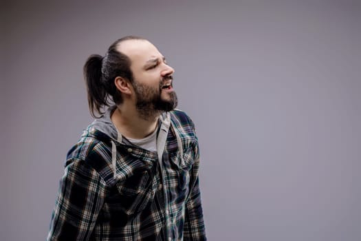 Young man with a beard and ponytail grimaces in pain, looking up and to the side, showing discomfort and agony