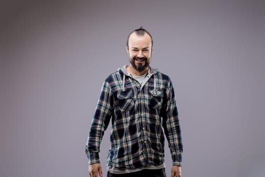 Smiling man in a plaid shirt exudes happiness and confidence in a studio with a gray background, showcasing a casual yet stylish look