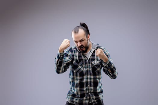 Young man is expressing negative emotions with an intense expression on his face, clenching his fists and opening his mouth wide