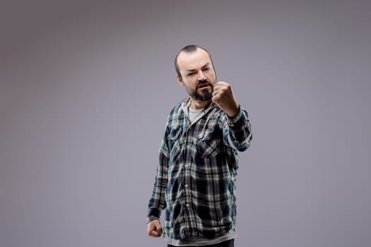 Adult man with a beard is clenching his fists and showing aggression, expressing negative emotions such as anger and rage