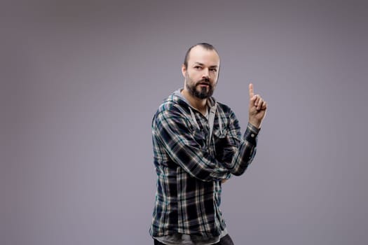 Confident bearded man pointing up with a brilliant idea, looking serious and trustworthy in plaid shirt against gray background