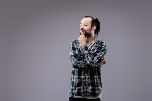 Young man with a beard is touching his beard and thinking with a thoughtful expression on his face, deep in contemplation