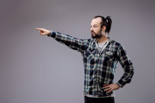 Bearded man pointing accusingly, hand on hip, with a serious expression showing conflict, frustration, and anger, exuding assertiveness and confidence against a gray background