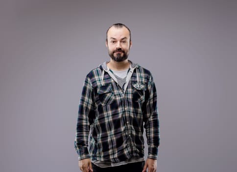 Confident man in plaid shirt standing against grey background, conveying seriousness and thoughtfulness. Shows healthy lifestyle and casual style