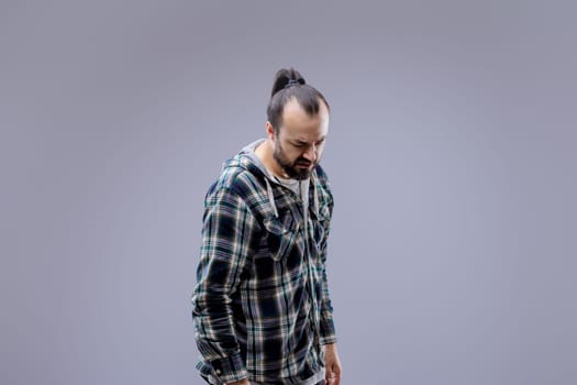 Man with a beard and a man bun looks down, showing pain and discomfort. His sad expression reflects backache, highlighting the need for healthcare