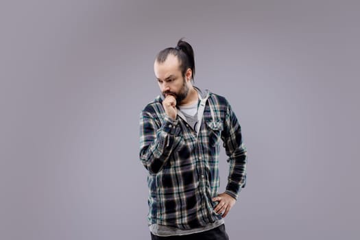 Bearded man with a ponytail is deep in thought, touching his beard as he contemplates something with a serious expression