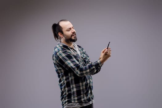 Man in his 30s, looking unhappy, reading bad news on his smartphone against a gray background