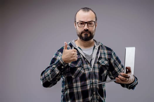 Confident technician holding laptop, giving thumbs up for successful cyber security solution. Expert ensures data safety in office setting
