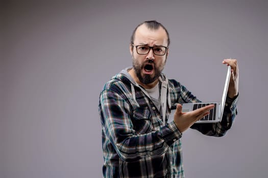 Frustrated technician screaming and holding laptop, overwhelmed by technology issues like errors, glitches, and viruses