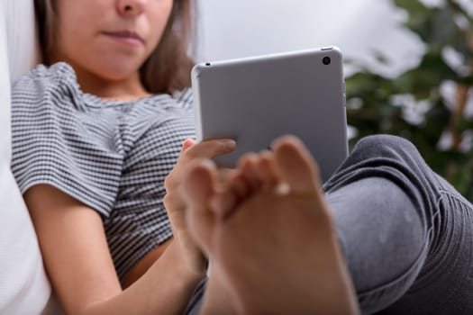 Young woman browsing online on a tablet while relaxing at home, immersed in modern technology for leisure and communication