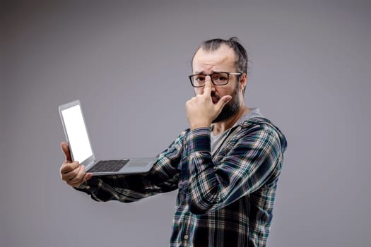Worried technician troubleshoots a laptop error in a gray studio, highlighting the challenges of technology and the need for support in computer repair