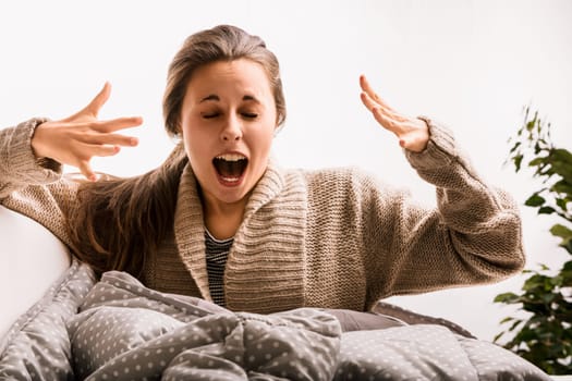 Young woman with long brown hair yawns and stretches in bed, starting her day in a cozy bedroom filled with natural light