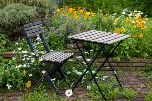 wild garden - herb spiral in the garden with fresh herbs and flowers, table and chair