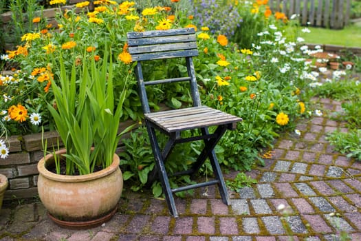 wild garden - herb spiral in the garden with fresh herbs and flowers and old chair