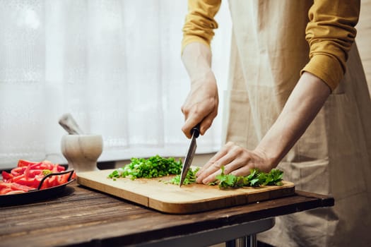 Unrecognizable man chopping cilantro with kitchen knife in the kitchen
