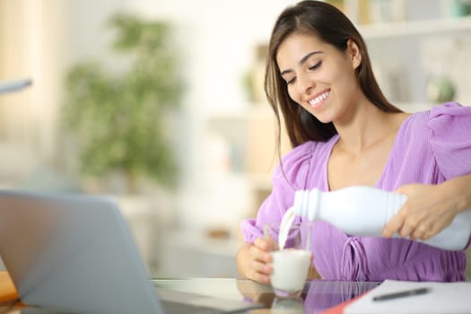 Happy student filling glass of milk e-learning at home