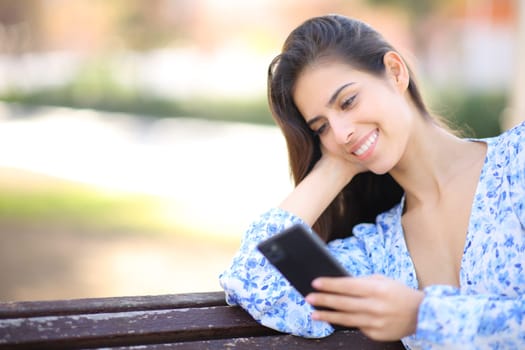 Happy female sitting on a bench reading phone message