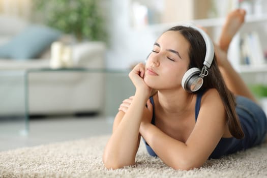 Relaxed woman listening music on headphone lying on a carpet at home