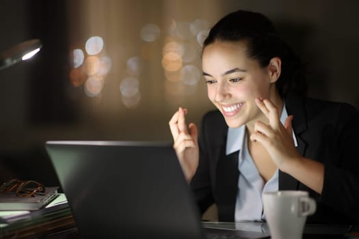 Happy executive working in the night crossing fingers checking laptop