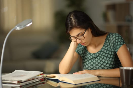 Woman with eyeglasses at home reading a book in the night on a desk