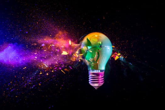 Broken light bulb exploding with colorful powder on a black background
