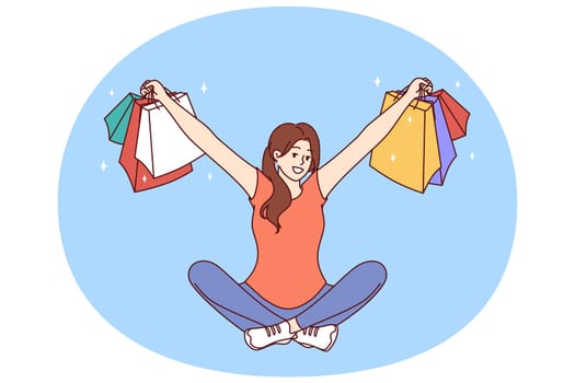 Woman with multi-colored packages from clothing stores sits with her arms apart after successful shopping. Girl who won shopping lottery shows off things purchased at big discount or cashback