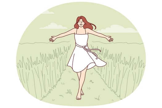 Woman walks along path among tall grass enjoying beautiful nature in rural or farming area. Girl in dress enjoys walk in wild nature or agricultural field in ecologically clean place.