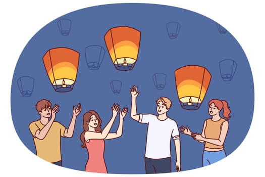 Group of people launch aerial chinese lanterns while making cherished wishes during traditional festival. Young friendly men and women with air lanterns celebrate chinese new year.
