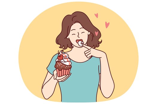Woman eats delicious cupcake, licking sweet cream from finger and enjoying appetizing dessert bought in craft bakery. Beautiful girl having lunch with cupcake with fresh berries from cake shop