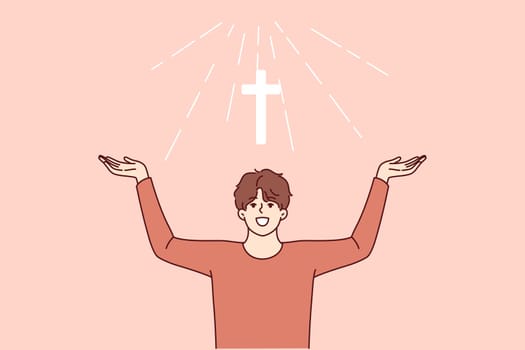 Man with christian cross above head rejoices at light coming from heaven and calls to visit church for prayers. Christian guy believes in miracle obtained by attending religious masses.
