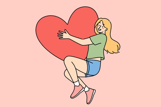 Happy teenage girl hugs large heart-shaped valentine card, rejoicing at coming of february holiday. Woman in love feels euphoria and romantic mood after receiving valentine day gift