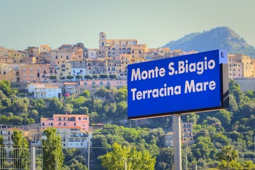 Signboard of the Monte San Biagio / Terracina Mare train station in Italy, with the town in the background.