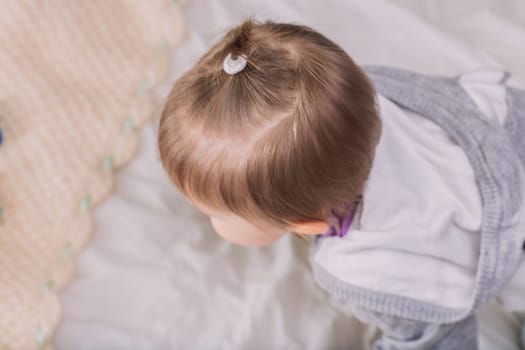 Baby girl with pigtails plays happily on a cozy bed, surrounded by soft blankets, embodying childhood innocence and joy