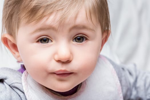 Sweet baby girl captures attention with direct eye contact, wearing an adorable bib. Natural light enhances expressive features, highlighting healthy growth and development