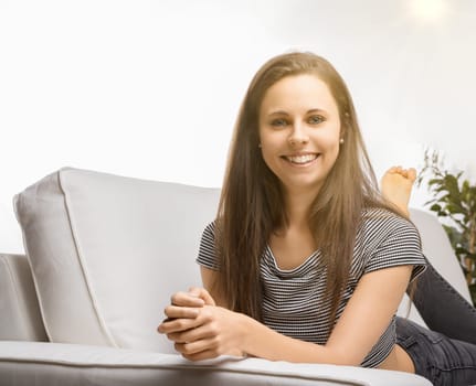 Young woman smiles happily on her couch at home, enjoying a relaxing day. She exudes a carefree vibe, basking in the serenity of her living room