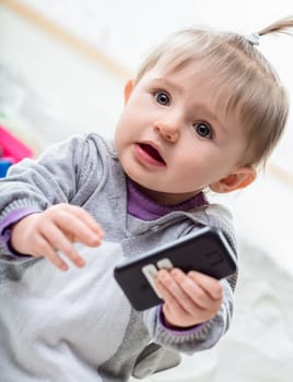 Baby girl holds a smartphone, looking surprised and curious, exploring the digital world with wonder and joy