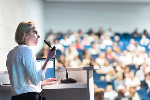 Female speaker giving a talk on corporate business conference. Unrecognizable people in audience at conference hall. Business and Entrepreneurship event